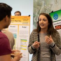 A student speaks to a guest about her poster presentation